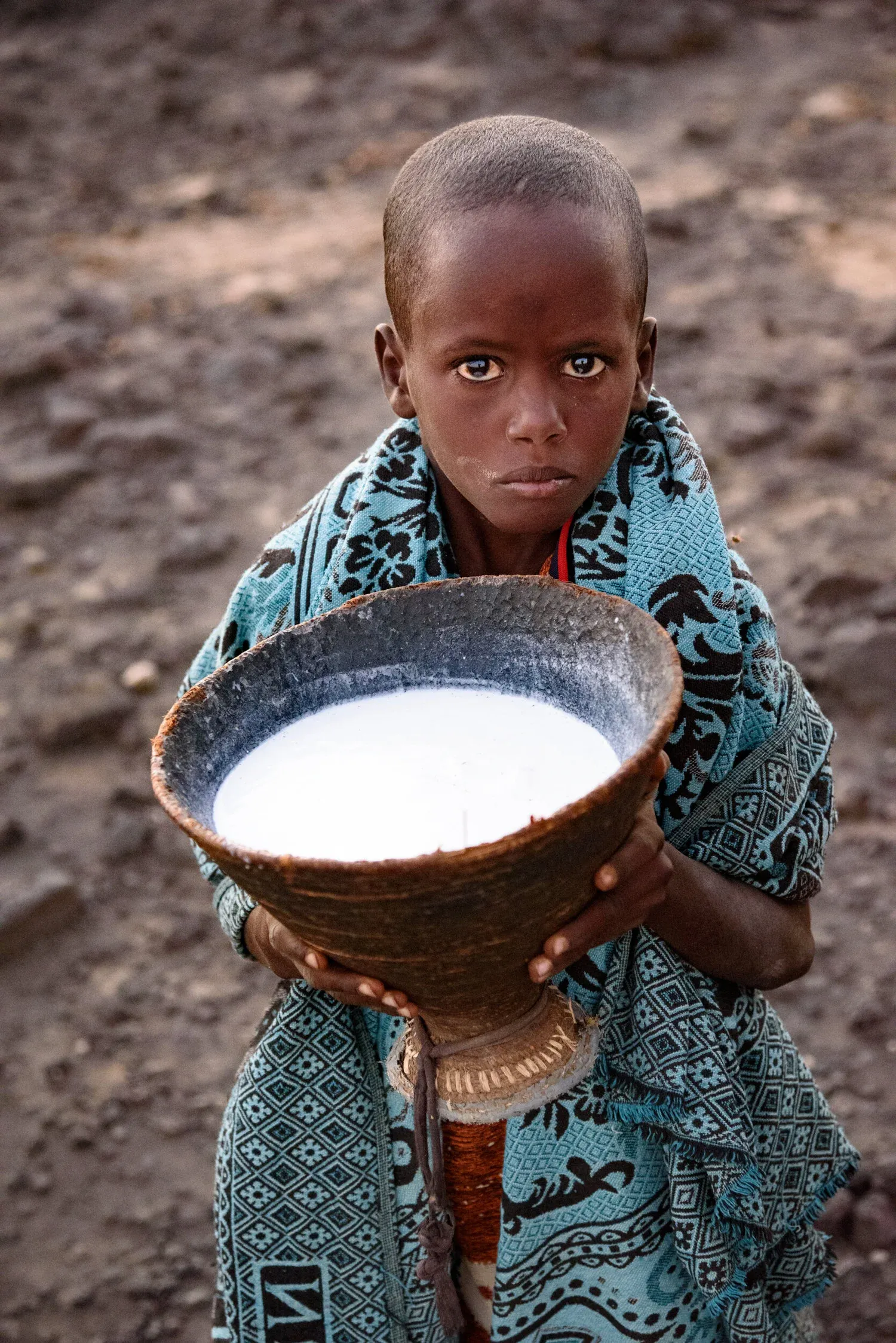 A young Afar boy holding a woven bowl of milk