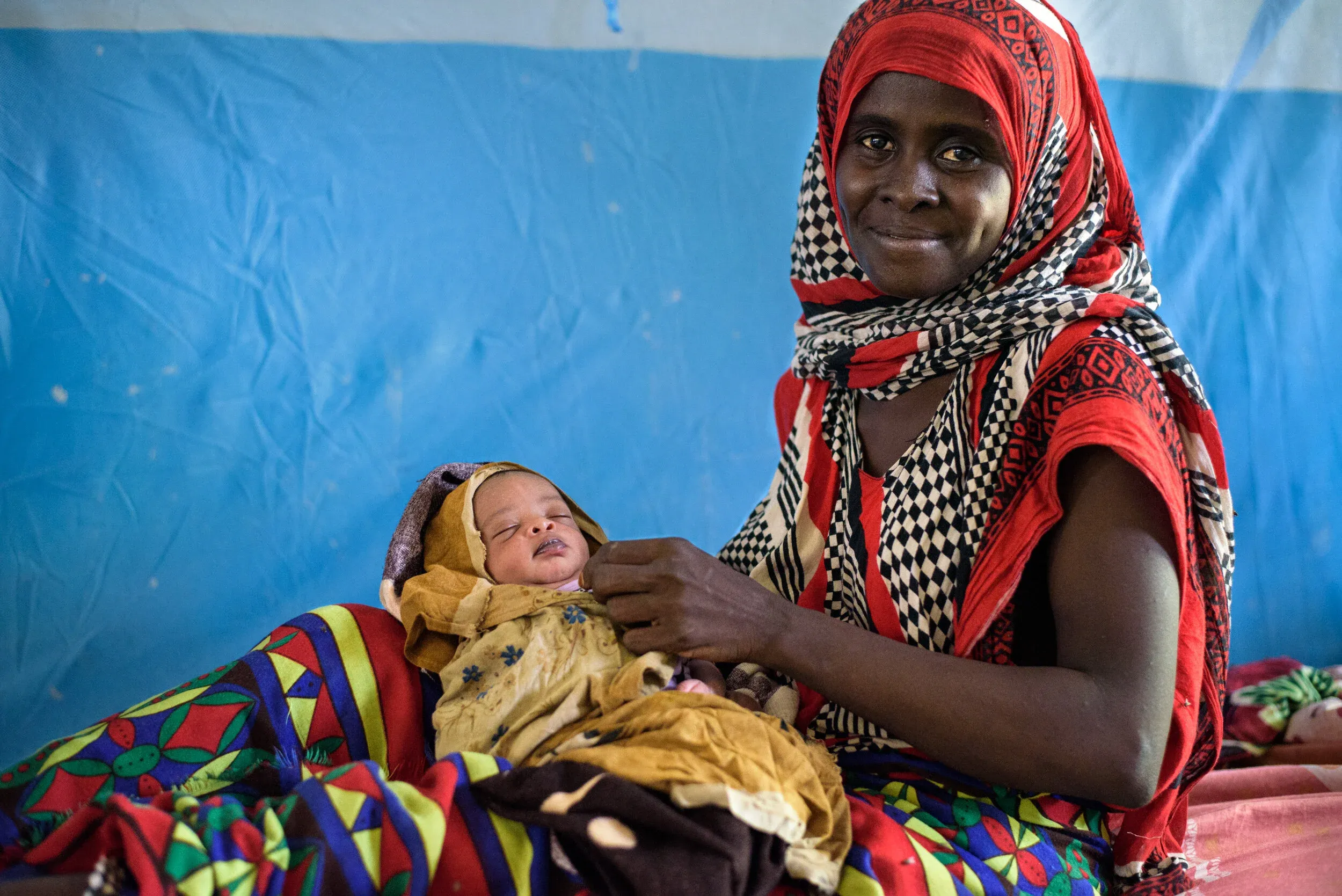 A mother smiling as she holds her sleeping newborn baby