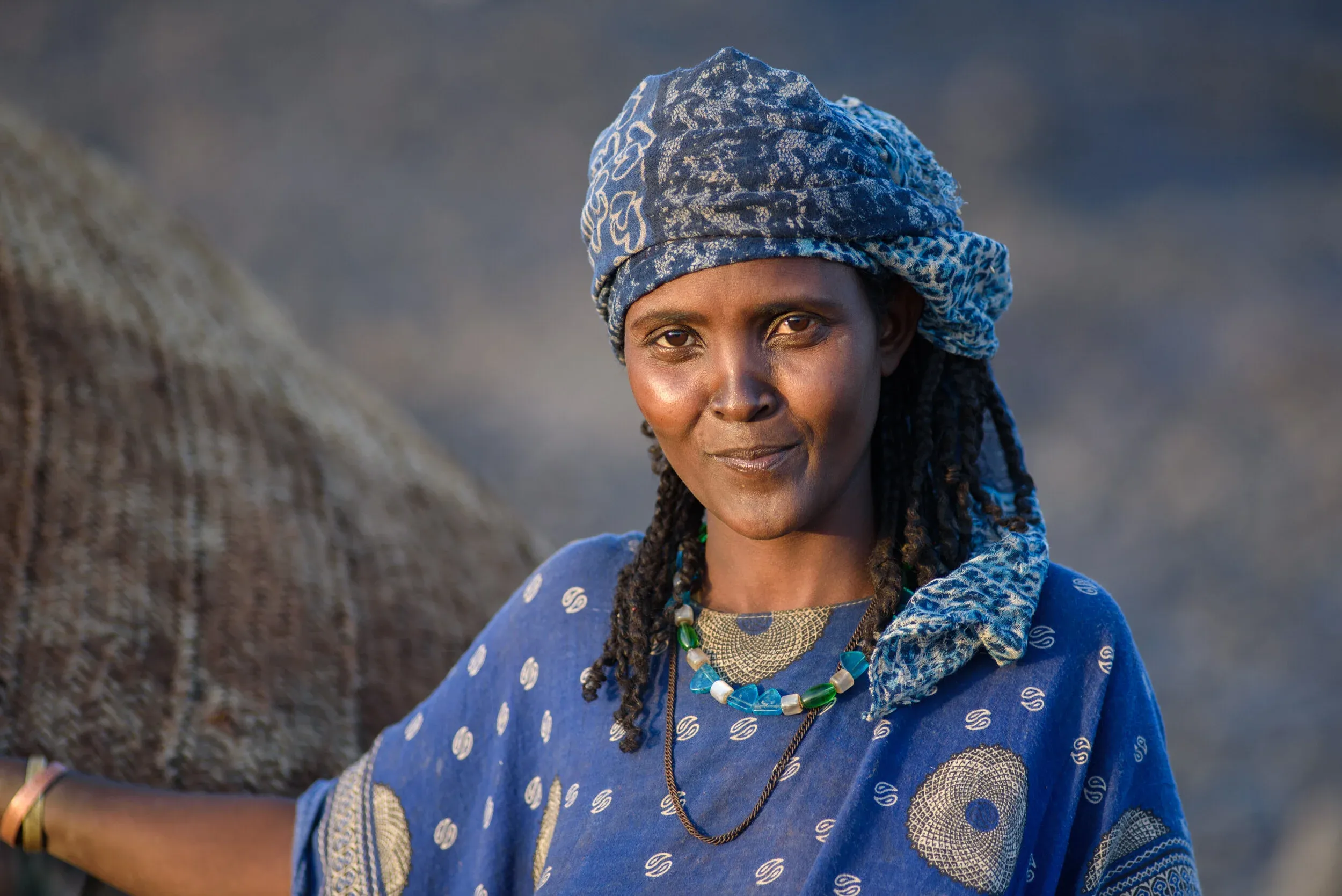 A smiling Afar woman wearing a blue headscarf and a beaded necklace