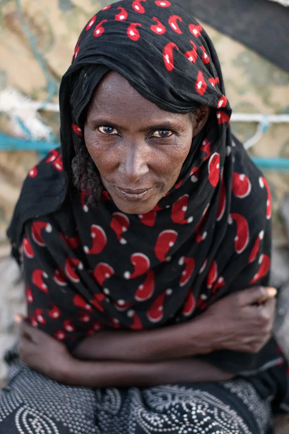 An Afar woman in a black and red headscarf, arms folded, looking into the camera